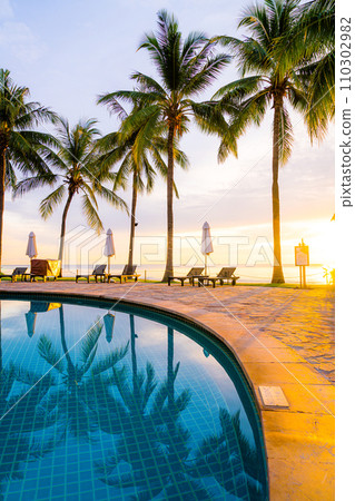 Umbrella and chair around swimming pool in hotel resort with sunrise in morning Umbrella and chair around swimming pool in hotel resort with sunrise in morning 110302982