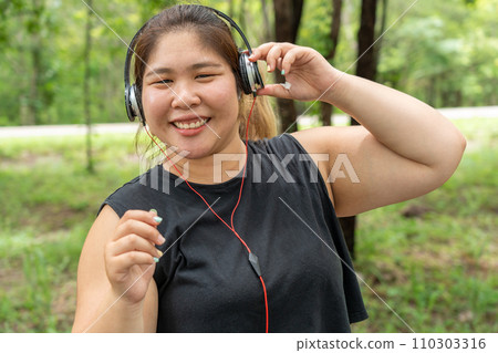 Happy over size Asian woman listening to music from her headphone at a local park Happy over size Asian woman listening to music from her headphone at a local park 110303316
