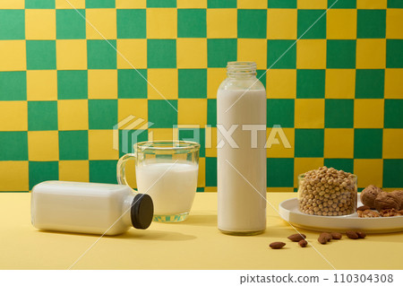 Two bottle and a mug of fresh milk decorated with a ceramic dish containing different types of nuts and soybeans. The protein in soy milk is healthy Two bottle and a mug of fresh milk decorated with a ceramic dish containing different types of nuts and soybeans. The protein in soy milk is healthy 110304308