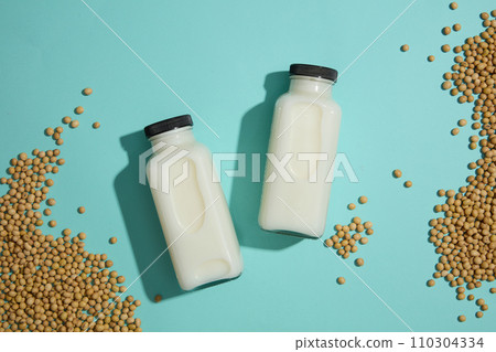 Top view of a lot of soybeans decorated over light background with milk bottles. Template for mockup your design. Concept of organic foods advertising Top view of a lot of soybeans decorated over light background with milk bottles. Template for mockup your design. Concept of organic foods advertising 110304334