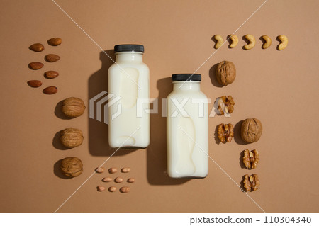Against brown background, two blank label milk bottles and some different types of nut. View from above. Nuts and beans are essential for overall health Against brown background, two blank label milk bottles and some different types of nut. View from above. Nuts and beans are essential for overall health 110304340