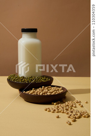 Wooden dishes containing green beans and soybeans. Blank label milk bottle displayed. The texture of soy drink can be combined with different fruits 110304359