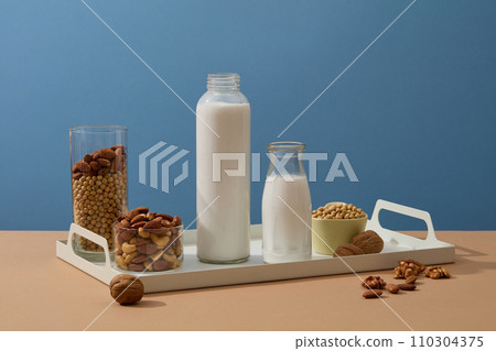 White tray featured empty label milk bottles with soybeans, almond and walnuts. Blue background. Research suggests that nuts and beans may reduce inflammation 110304375
