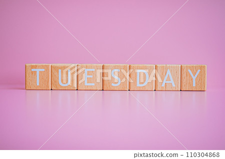 Wooden blocks form the text "TUESDAY" against a pink background. 110304868