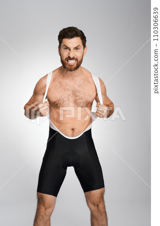 Angry bearded wrestler in black and white singlet, while posing to camera. Front view of aggressive athlete making face, showing rage, isolated on white studio background. Concept of wrestling. Angry bearded wrestler in black and white singlet, while posing to camera. Front view of aggressive athlete making face, showing rage, isolated on white studio background. Concept of wrestling. 110306639