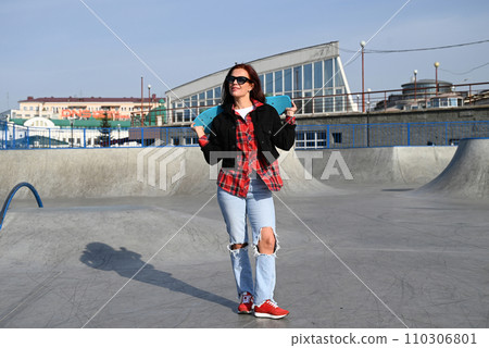 An active middle-aged woman rides a skateboard on an empty road or highway. An ordinary city woman relaxing on a skateboard after work. The concept of a modern lifestyle An active middle-aged woman rides a skateboard on an empty road or highway. An ordinary city woman relaxing on a skateboard after work. The concept of a modern lifestyle 110306801