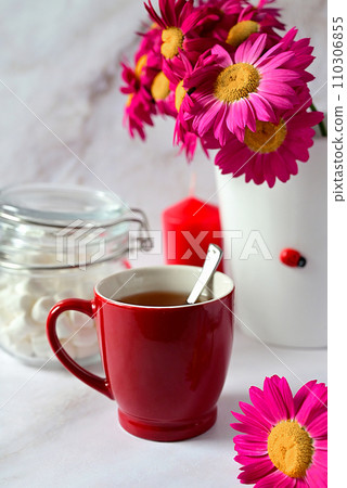 red mug with tea on the background of a bouquet of red flowers red mug with tea on the background of a bouquet of red flowers 110306855