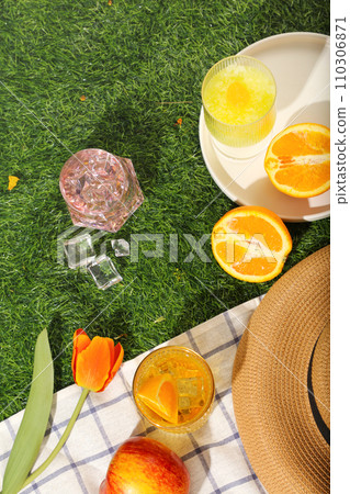 Picnic set with checkered fabric, fresh fruit, cups of cocktail and flower on green grass background. Top view, concept of happy summer day 110306871