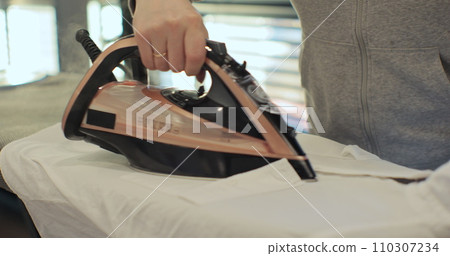 Close up of female hands ironing clothes with iron on an ironing board. Close up of female hands ironing clothes with iron on an ironing board. 110307234