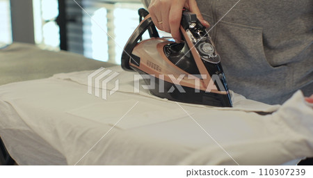 Close up of female hands ironing clothes with iron on an ironing board. Close up of female hands ironing clothes with iron on an ironing board. 110307239