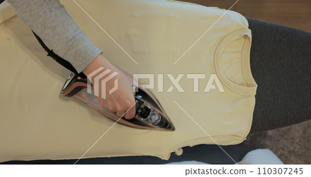 View from above female using electric iron for ironing clothes at home housework. Home routine housekeeping. View from above female using electric iron for ironing clothes at home housework. Home routine housekeeping. 110307245