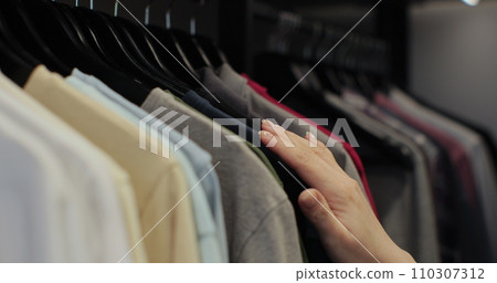 Woman in the shop looks through the male clothes, which are hanging on the racks. Home closet or wardrobe. 110307312