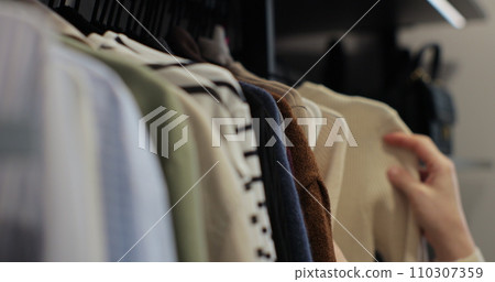 Woman choosing clothes from rack with hangers inside room. Lady looks to clothes, decides what to wear. Lifestyle women relax at home concept. 110307359