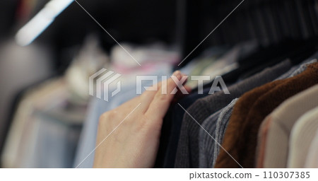 Woman hand runs across a rack of clothes at house or store. Home wardrobe or clothing shop changing room. Woman hand runs across a rack of clothes at house or store. Home wardrobe or clothing shop changing room. 110307385