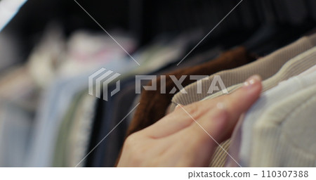 Woman hand runs across a rack of clothes at house or store. Home wardrobe or clothing shop changing room. Woman hand runs across a rack of clothes at house or store. Home wardrobe or clothing shop changing room. 110307388