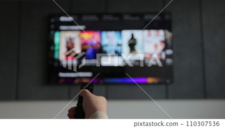 Woman hand operating a remote control for a smart TV. Channel surfing, focused on the hand and remote control. 110307536