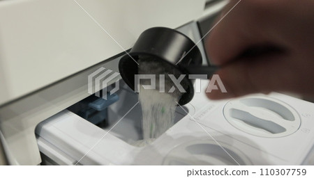 Woman pours washing powder into the washing machine compartment. Female with measuring spoon, fills the washing machine with powder. Woman pours washing powder into the washing machine compartment. Female with measuring spoon, fills the washing machine with powder. 110307759