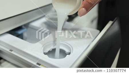 Pour laundry gel softener to smell good into the washing machine container. Using fabric softener for laundry. Household chores concept. Pour laundry gel softener to smell good into the washing machine container. Using fabric softener for laundry. Household chores concept. 110307774
