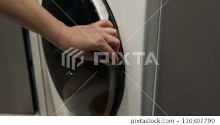 Woman pulls clean washed clothing from the washing machine. Washing clothing in domestic washing machine. Woman pulls clean washed clothing from the washing machine. Washing clothing in domestic washing machine. 110307790