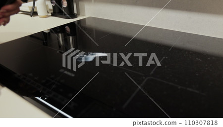 Cleaning induction electric stove with cleaning spray at kitchen countertop. Woman cleaning house, cleaning service. Cleaning induction electric stove with cleaning spray at kitchen countertop. Woman cleaning house, cleaning service. 110307818