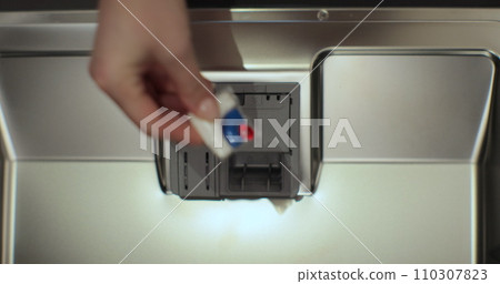 Close-up, top view. Woman putting an all in one detergent capsule pill into a dishwasher. 110307823