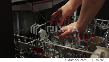 Woman takes a washed glasses from dishwasher machine. Household domestic life. Close-up, top view. Woman takes a washed glasses from dishwasher machine. Household domestic life. Close-up, top view. 110307858