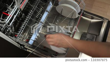 Woman takes a washed plate from dishwasher machine. Household domestic life. Close-up, top view. Woman takes a washed plate from dishwasher machine. Household domestic life. Close-up, top view. 110307875