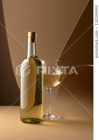 Bottle and glass of white wine on a beige background. Bottle and glass of white wine on a beige background. 110308402