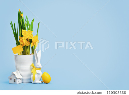 Yellow Easter eggs in a nest and blooming daffodils in a white pot and Easter bunny with tiny house on blue background. Happy Easter wide web banner 110308888