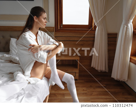 Young woman on bed brunette woman wrapped in white blanket at home in the morning. Sensual young woman with sexy body in shirt and white lingerie in modern apartment after waking up. weekend, vacation 110312474