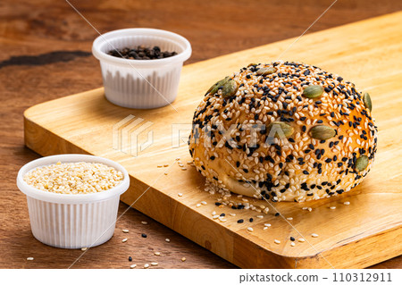 High angle view of homemade burger bun sprinkled with white and black sesame and pumpkin seeds. 110312911
