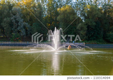The magical beauty of the autumn park with a fountain on the pond brings peace and quiet The magical beauty of the autumn park with a fountain on the pond brings peace and quiet 110314094