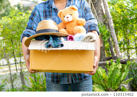 Volunteer woman provide clothing donation box with used clothes and doll to support help for refugee, homeless or poor people in the world. Volunteer woman provide clothing donation box with used clothes and doll to support help for refugee, homeless or poor people in the world. 110315402
