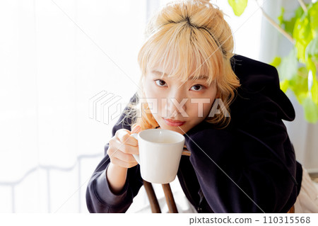 金髮女郎向後坐在椅子上喝咖啡 金髮女郎向後坐在椅子上喝咖啡 110315568