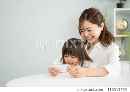 Mother and daughter enjoy watching videos on smartphone together Mother and daughter enjoy watching videos on smartphone together 110315793