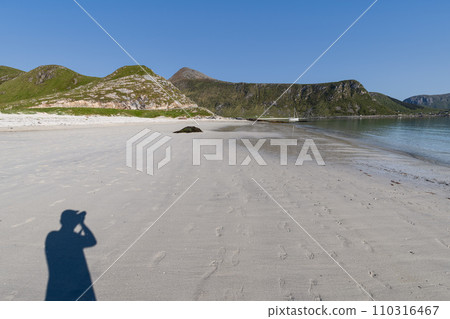 Photographer on Haukland Beach's sands with a yacht in calm bay, Lofoten 110316467