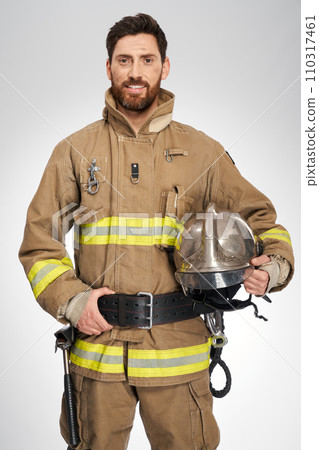 Handsome caucasian firefighter smiling to camera indoors. Portrait of happy, strong male fireman in protective uniform holding helmet, on white studio background. Workplace, safety concept. Handsome caucasian firefighter smiling to camera indoors. Portrait of happy, strong male fireman in protective uniform holding helmet, on white studio background. Workplace, safety concept. 110317461