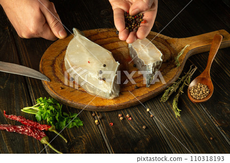 Close-up of a man hands adding dry pepper to Anarhichas fish before frying. Concept of delicious fish diet at home Close-up of a man hands adding dry pepper to Anarhichas fish before frying. Concept of delicious fish diet at home 110318193