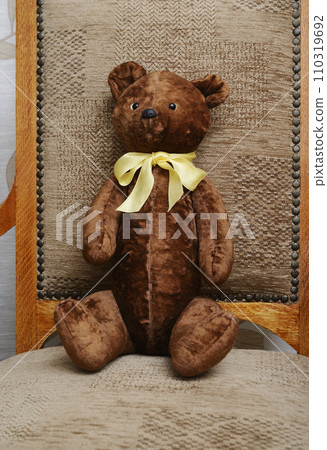 shabby teddy bear with a yellow bow on his neck sitting in an old armchair 110319692