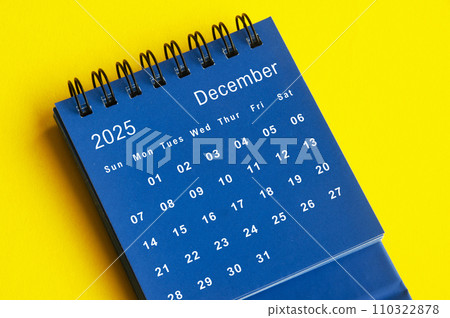 December 2025 blue desk calendar on yellow cover background. 110322878