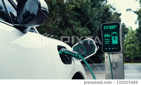 Electric car plugged in with charging station in eco green park. Peruse 110325489