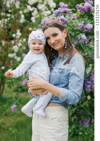 Young mother holds her baby son in her arms in a spring blooming lilac park Young mother holds her baby son in her arms in a spring blooming lilac park 110329256