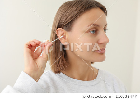 woman holds in hand disposable cotton bud, swab, stick. Girl cleans, washes her auricle earwax. Personal hygiene and care product. Prevention of ear diseases. Sulfur plug removal. 110332477