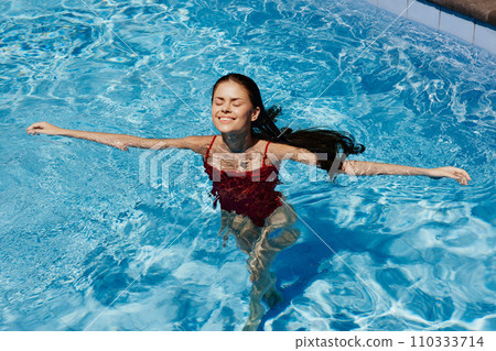 Happy woman swimming in pool in red swimsuit with loose long hair in sunshine, skin protection with sunscreen, concept of relaxing on vacation in tropical climate. Happy woman swimming in pool in red swimsuit with loose long hair in sunshine, skin protection with sunscreen, concept of relaxing on vacation in tropical climate. 110333714
