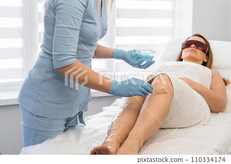 The process of applying moisturizing and protective cream on the skin feet. A professional cosmetologist in beauty salon performs photoepilation to achieve smooth and beautiful skin on woman's body. The process of applying moisturizing and protective cream on the skin feet. A professional cosmetologist in beauty salon performs photoepilation to achieve smooth and beautiful skin on woman's body. 110334174