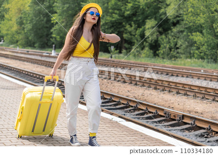 A view of tomorrow: a woman with a suitcase in yellow clothes and blue glasses gazes into a future full of adventure. Time to go: the image of a traveler in yellow clothing style, with a suitcase and 110334180