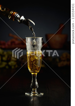 Yellow herbal liquor is poured from a vintage bottle into a glass. 110334431