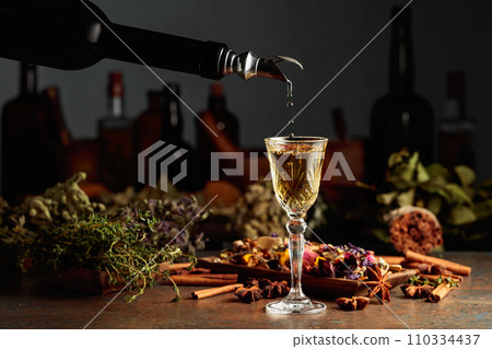 Yellow herbal liquor or mixture is poured from a vintage bottle into a glass. 110334437
