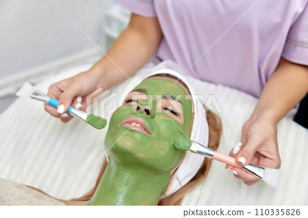 female beautician applies the mask to the face of beautiful woman in the spa salon. facial skin care 110335826