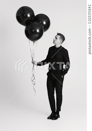 elegant caucasian man with bunch of black air balloons on white background. black and white elegant caucasian man with bunch of black air balloons on white background. black and white 110335841